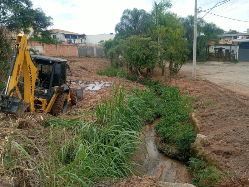 Máquina de escavação trabalhando em área com vegetação ao lado de um pequeno rio.