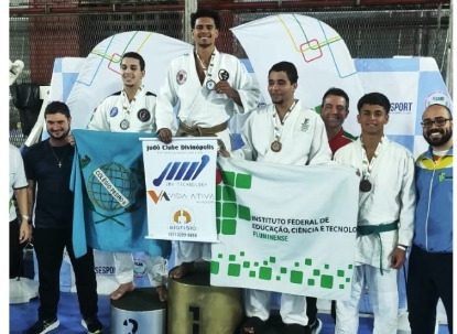 Vencedores de um torneio de judô segurando medalhas e bandeiras, posando no pódio.