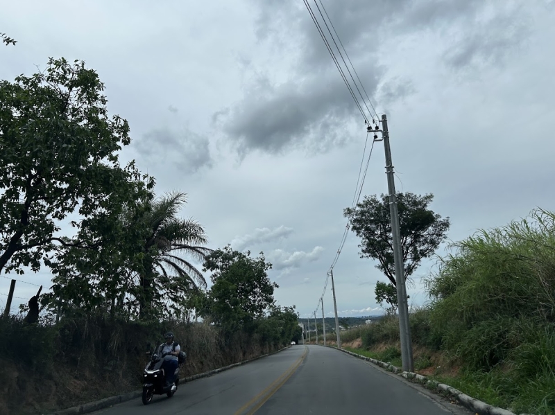 Uma motocicleta percorre uma estrada rodeada por árvores e arbustos sob um céu nublado.