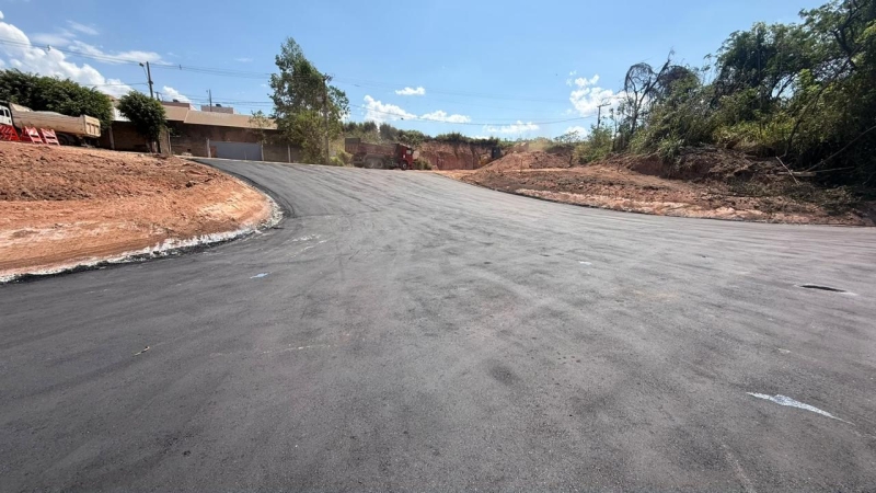 Vista de uma estrada recém-pavimentada em uma curva, com árvores e terreno ao fundo.
