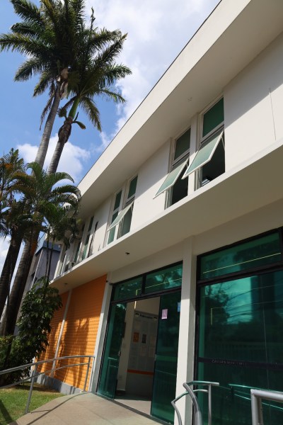 Fachada de um edifício moderno com palmeiras ao redor, janelas abertas e entrada acessível.