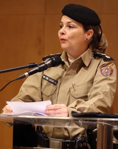 Mulher em uniforme militar falando ao microfone durante um evento, com um olhar sério e concentrado.
